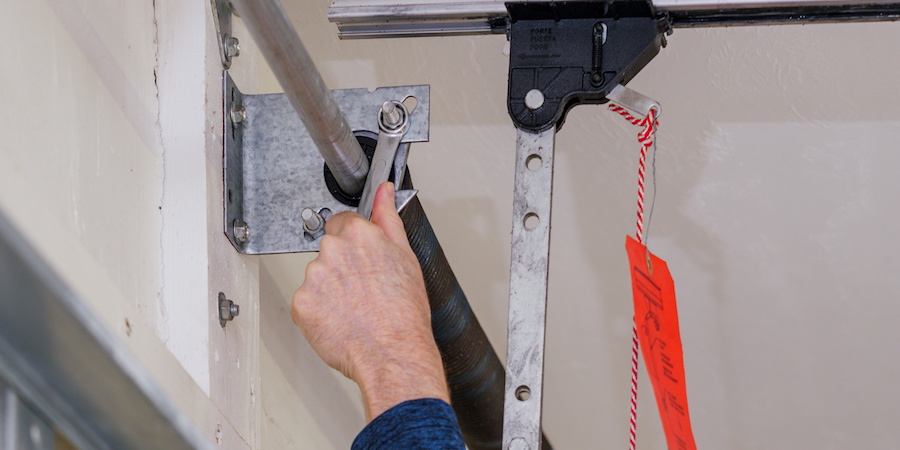 Man tightening nuts and bolts on a garage door system.