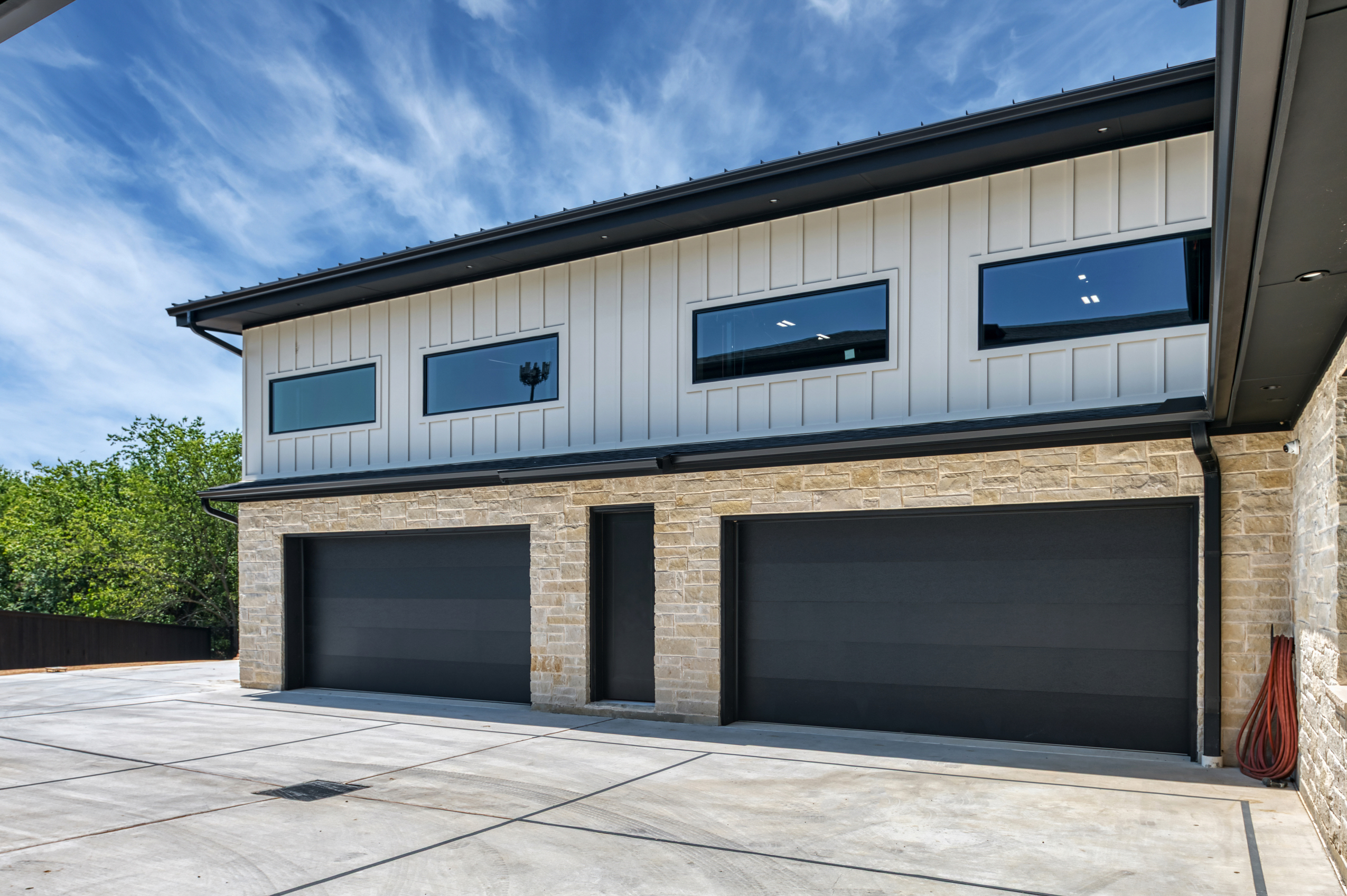 black garage doors with stone and white board and batten siding